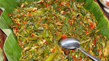 Geleneksel Endonezya usulü kızarmış su ıspanağını biberli ve ançüezli muz yaprağında servis et. Orijinal Asya mutfağı, baharatlı sebze yemeği, sağlıklı sokak yemekleri sunumu..
