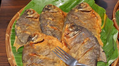 Bambu tepsisinde muz yaprakları üzerinde geleneksel Endonezya kızarmış balıklarına yakın çekim. Orijinal Asya mutfağı sunumu, çıtır çıtır doku, kültürel gıda geçmişi, editoryal kullanım için mükemmel..