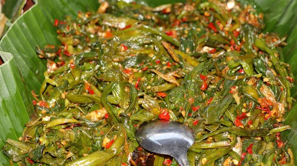 Geleneksel Endonezya usulü kızarmış su ıspanağını biberli ve ançüezli muz yaprağında servis et. Orijinal Asya mutfağı, baharatlı sebze yemeği, sağlıklı sokak yemekleri sunumu..