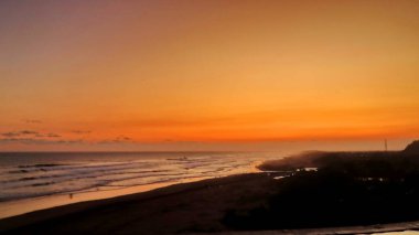Altın turuncu gökyüzü, okyanus dalgaları ve akşamdan zevk alan insanların siluetleri ile güzel tropikal plaj günbatımı. Seyahat, turizm ve doğa için mükemmel sakin bir sahil manzarası..