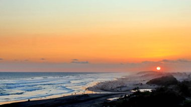 Altın turuncu gökyüzü, okyanus dalgaları ve akşamdan zevk alan insanların siluetleri ile güzel tropikal plaj günbatımı. Seyahat, turizm ve doğa için mükemmel sakin bir sahil manzarası..