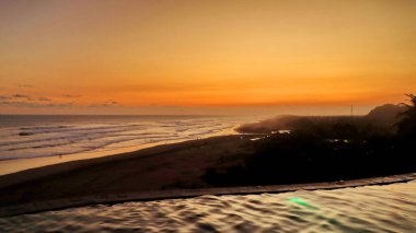 Altın turuncu gökyüzü, okyanus dalgaları ve akşamdan zevk alan insanların siluetleri ile güzel tropikal plaj günbatımı. Seyahat, turizm ve doğa için mükemmel sakin bir sahil manzarası..