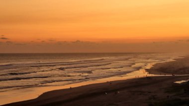 Altın turuncu gökyüzü, okyanus dalgaları ve akşamdan zevk alan insanların siluetleri ile güzel tropikal plaj günbatımı. Seyahat, turizm ve doğa için mükemmel sakin bir sahil manzarası..