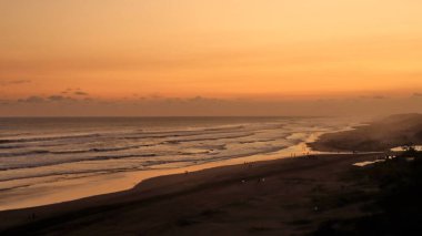 Altın turuncu gökyüzü, okyanus dalgaları ve akşamdan zevk alan insanların siluetleri ile güzel tropikal plaj günbatımı. Seyahat, turizm ve doğa için mükemmel sakin bir sahil manzarası..