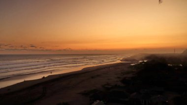 Altın turuncu gökyüzü, okyanus dalgaları ve akşamdan zevk alan insanların siluetleri ile güzel tropikal plaj günbatımı. Seyahat, turizm ve doğa için mükemmel sakin bir sahil manzarası..