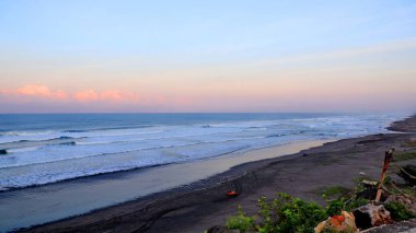 Tropikal plajın çarpıcı deniz manzarası kıyıya vuran dalgalar, dramatik sahil kayalıkları ve günbatımında pastel gökyüzü. Seyahat, doğa ve manzara için mükemmel..