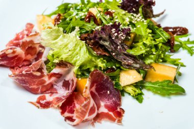 prosciutto ve ahşap bir masa üzerinde beyaz bir tabak içinde mango salatası