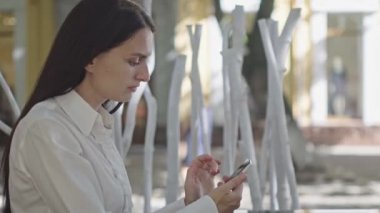 güneşli gün, yeşil ağaçların bir arka plan karşı bir restoran yaz oyun bir telefon ile güzel esmer iş kadını