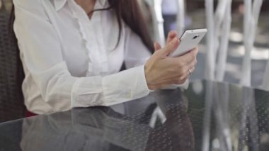 güneşli gün, yeşil ağaçların bir arka plan karşı bir restoran yaz oyun bir telefon ile güzel esmer iş kadını