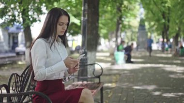 güneşli gün, güzel esmer iş kadını yeşil ağaçların bir arka plan karşı parkta telefonda konuşurken