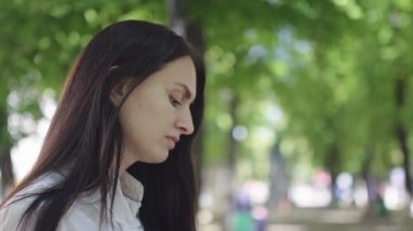 güneşli gün, güzel esmer iş kadını yeşil ağaçların bir arka plan karşı parkta telefonda konuşurken