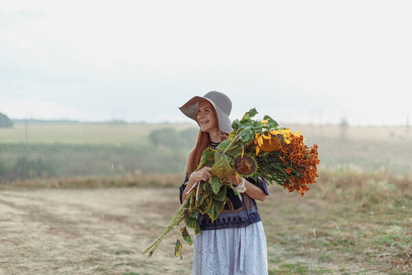 Red girl in a big hat with flowers in a field in the rain