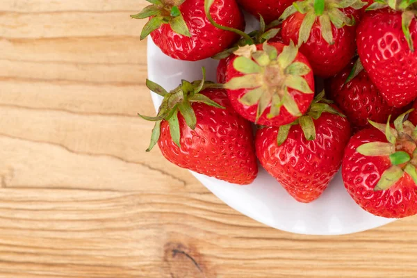 Tahta bir masada beyaz bir tabakta bir sürü taze çilek.
