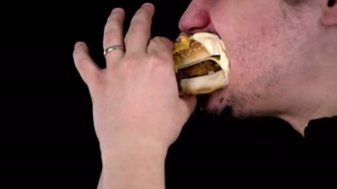 Genç evli adam tohumları ile kaplı ve tavuk burger ve koyun peyniri ile dolu lezzetli hamburger içine ısırır. Beyaz sause sakalında kalır.