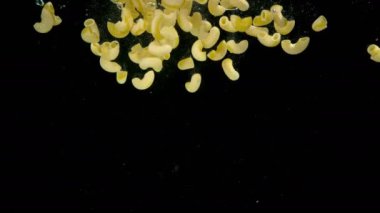 Küçük bükülmüş makarna yavaş yavaş kaynamış tuzlu suya düşüyor.