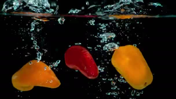 新鮮で有機的な赤とオレンジのピーマンは エレガントに新鮮な透明な水のポットに落ちる — ストック動画
