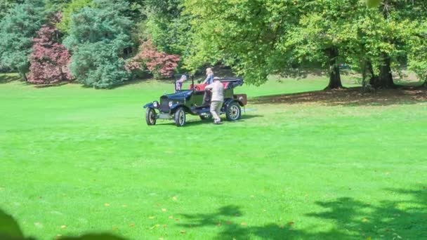 三个人正在从一辆老式汽车里出来 这辆车正站在一个美丽的绿色草坪上 — 图库视频影像