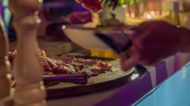 Siyah akşam elbisesi giyen sevimli genç esmer bir plaka zevkli prosciutto dilimleri koyarak.