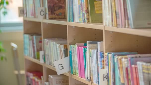 若い学生が図書館の棚のそばに立ち寄り 特定の本を探します 彼女のクラスメートは彼女を助けている — ストック動画