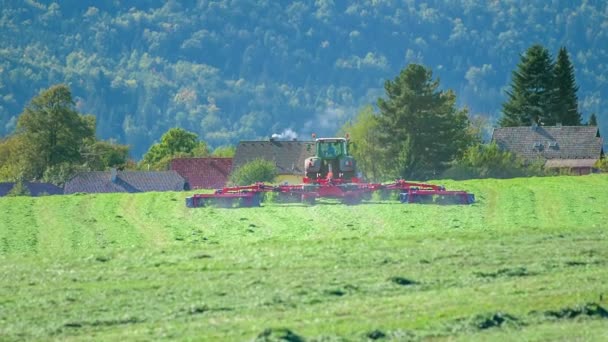 私たちは 丘を運転赤いトラクターを見ることができ それはその後ろに巨大な草の切断機械を引っ張っています 草原は巨大です — ストック動画