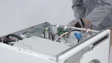 Tamirci gelişmiş çamaşır makinesinin elektronik devrelerini söküyor. Küçük bir batarya matkabına yardım ediyor..