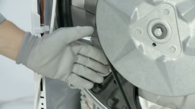 Tamirci, çamaşır makinesinin arka tarafına yerleştirilmiş vites kolunu yavaşça çıkarıyor..