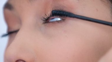 A young make up artist slowly applies mascara on the client's upper eyelashes.