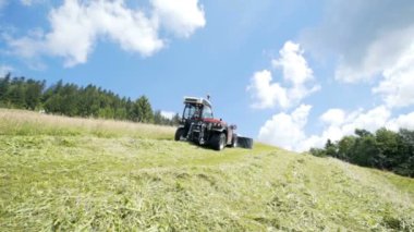 Bir traktör yokuş yukarı gidiyor ve gracc kesme makineleri ile çim kesiyor.