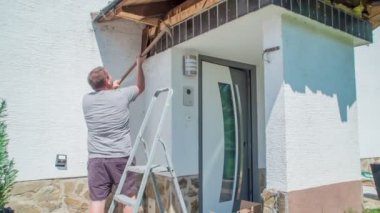 Genç adam çatının koyu kahverengi ahşap tahtalarını kaldırarak yapıyı yıkıyor. Kazmaya yardım ediyor..