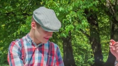 Genç bir kadın erkek arkadaşına çilek veriyor ve onu ısırıyor. Parkta dışarıda piknik yapıyorlar..