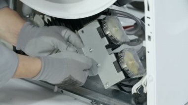 Tamirci, çamaşır makinesinin önemli bir kısmını tutan metal panelin vidalarını sökmeye hazırlanıyor..