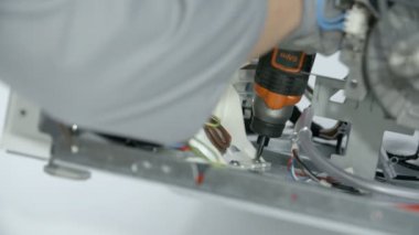 Tamirci çamaşır makinesini tamir ediyor. Çamaşır makinesinin bir parçasını tutan iki vidayı söküyor..