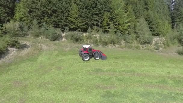 一辆红色的拖拉机在陡峭的山坡上行驶 它正用农业机械割草 空中拍摄 夏天是夏天 — 图库视频影像