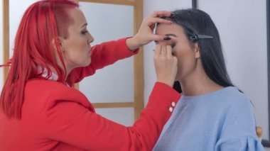Bir müşteri sandalyede oturuyor. Bir makyaj sanatçısı bir eyeliner ile bir çizgi çiziyor.