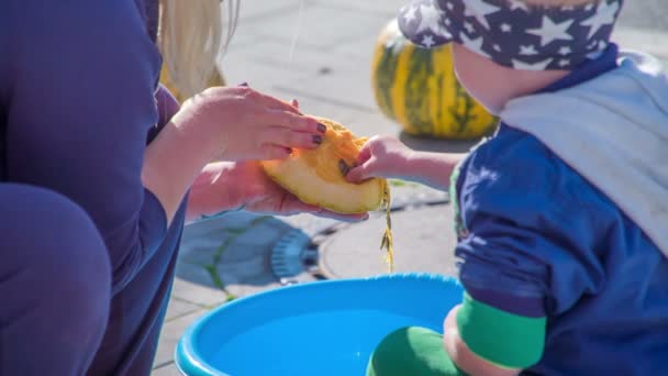 一个小男孩帮妈妈把南瓜种子放进一个蓝色的桶里 — 图库视频影像
