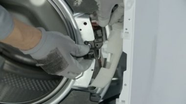 Tamirci, çamaşır makinesinin güvenlik kapısını açıp kapatan özel seçim bölümünü dikkatlice temizliyor..