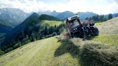 Bir traktör yokuş aşağı gidiyor ve çiftçi tarım makineleri ile saman hazırlanıyor.