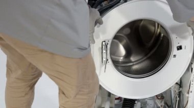 Profesyonel bir tamirci bozuk çamaşır makinesinin ön çember tahtasını kaldırıyor..