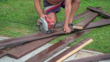 Yaşlı bir adam koyu kahverengi ahşap tahtayı çizgilere kesiyor. Kullanışlı bir testere yardımı..