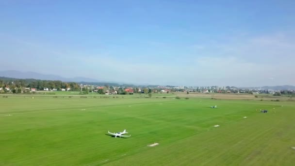 一架白色的小飞机在跑道上驾驶 跑道是用草做的 机场在一片美丽的风景区中间 — 图库视频影像