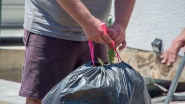 Adam küçük cam yünleri torbaya koyuyor. Diğer adam izolasyon malzemeleriyle dolu siyah bir poşet bağlayıp çöpe atıyor..