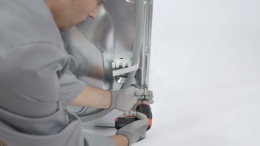 Bozuk çamaşır makinesinin arka tarafındaki vidaları söken proffesional tamirci küçük pilli matkapla çalışıyor..