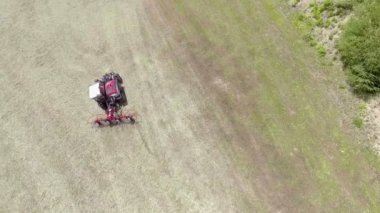 Hava görüntüsü. Dışarıda büyük bir çim tarlasında çalışan bir traktörü gözlemleyebiliriz. Yaz mevsimindeyiz ve çiftçilerin dışarıda yapacak çok işi var..