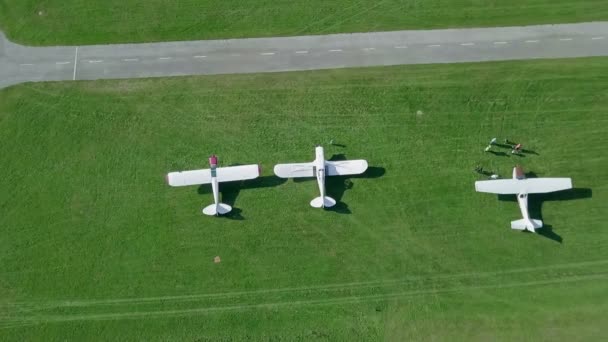 3機の小さな白い飛行機が緑の草の上に立っている すべてが緑です 晴れた日だ航空写真 — ストック動画