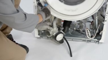 Erkek tamirci, çamaşır makinesinin kırık kısmından kabloları ve hortumları ayırmak için özel eğilmiş burun pensesi kullanıyor..