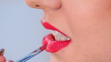 A make up artist colours the inner part of the client's lips. She uses a nice red colour to accentuate her lips.
