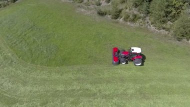 Kırmızı bir traktör çayırboyunca gidiyor. Hayvanlar için saman hazırlama nın zamanı. Havadan çekim.