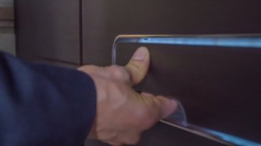 Bir işadamı evin ön kapısını açmak için bir kolu iter. Sonra içeri girer..
