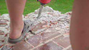 Uygunsuz ayakkabılar giyen adam beton yıkıcı çekiçle beton yapıyı tahrip ediyor..