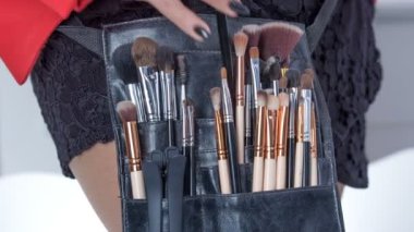 A make up artist takes one ofthe brushes out of the brush set and puts one of them back inside. Her brush set is around her waist.
